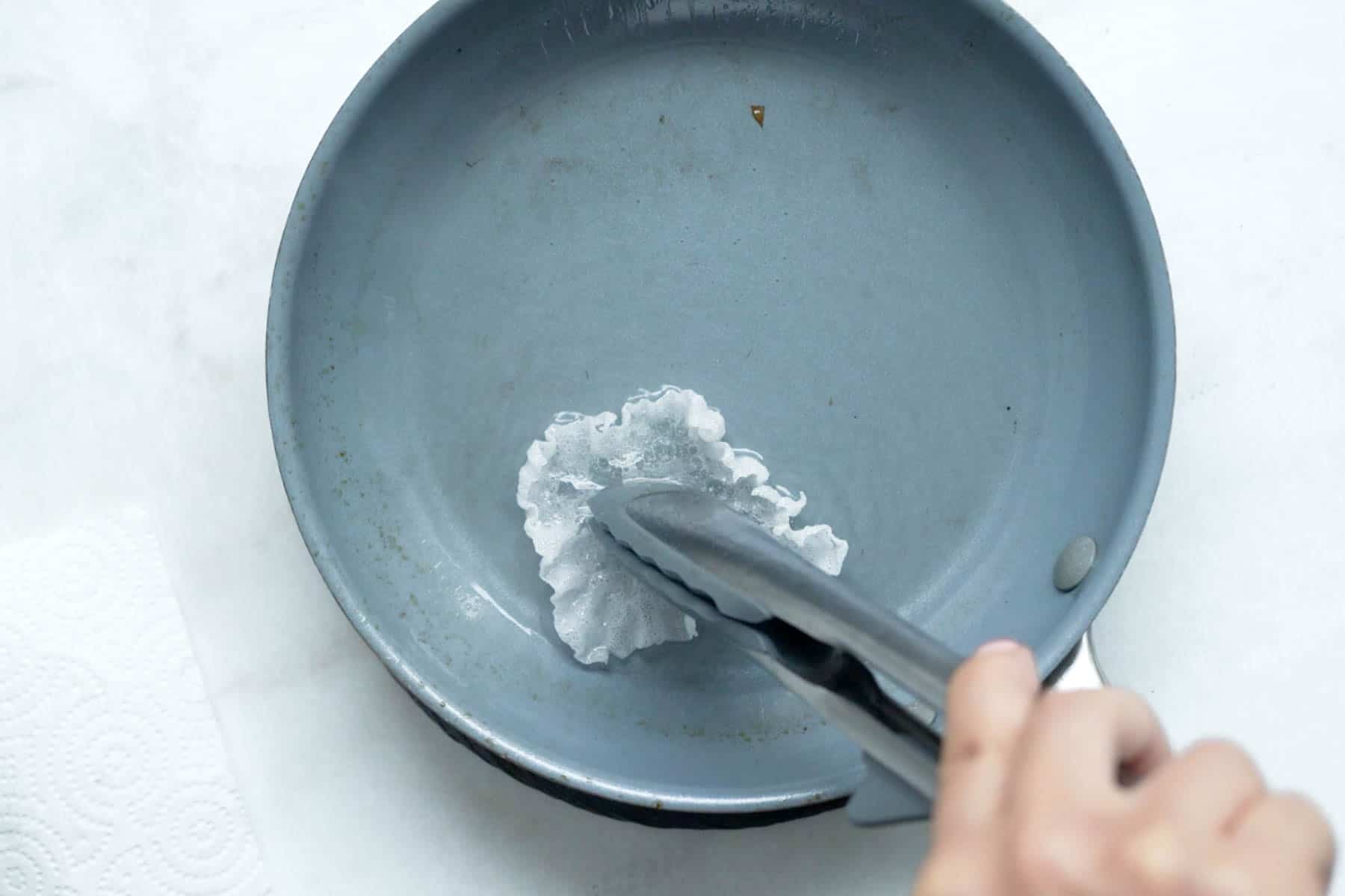 frying rice paper wrapper in a pan and holding middle with tongs.