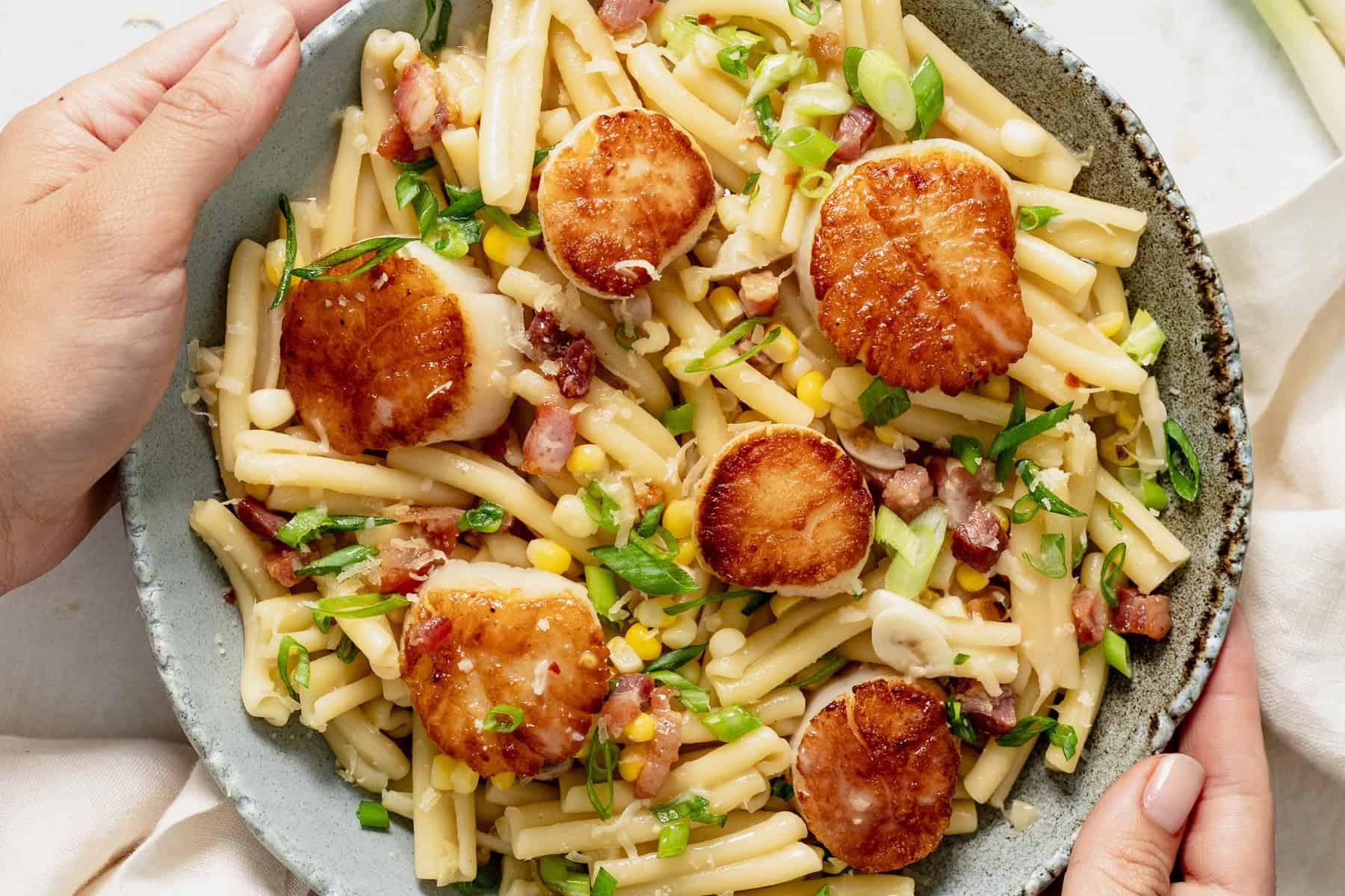 corn scallop pasta with white wine in bowl topped with scallions and pancetta.
