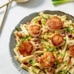 Seared scallops with pasta and bacon in a creamy sauce on a grey plate.