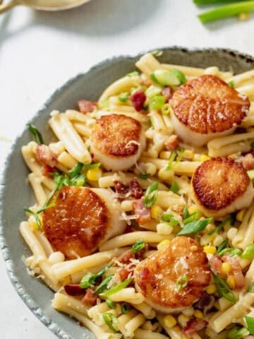 Seared scallops with pasta and bacon in a creamy sauce on a grey plate.