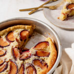 plum cardamom clafoutis in baking dish, with a slice on aplate with forks on the top right.