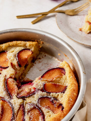 plum cardamom clafoutis in baking dish, with a slice on aplate with forks on the top right.