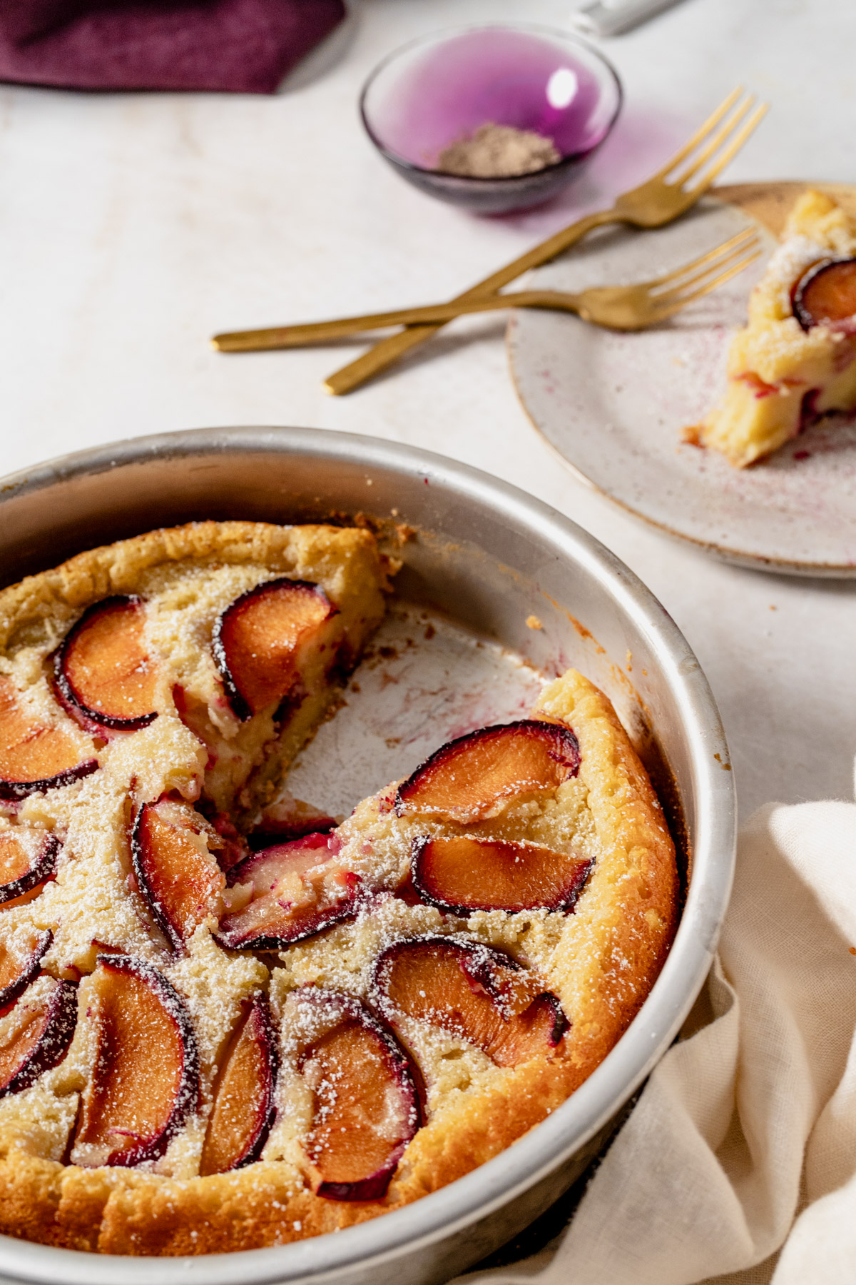 plum cardamom clafoutis in a pan, served slice with forks on the top right.