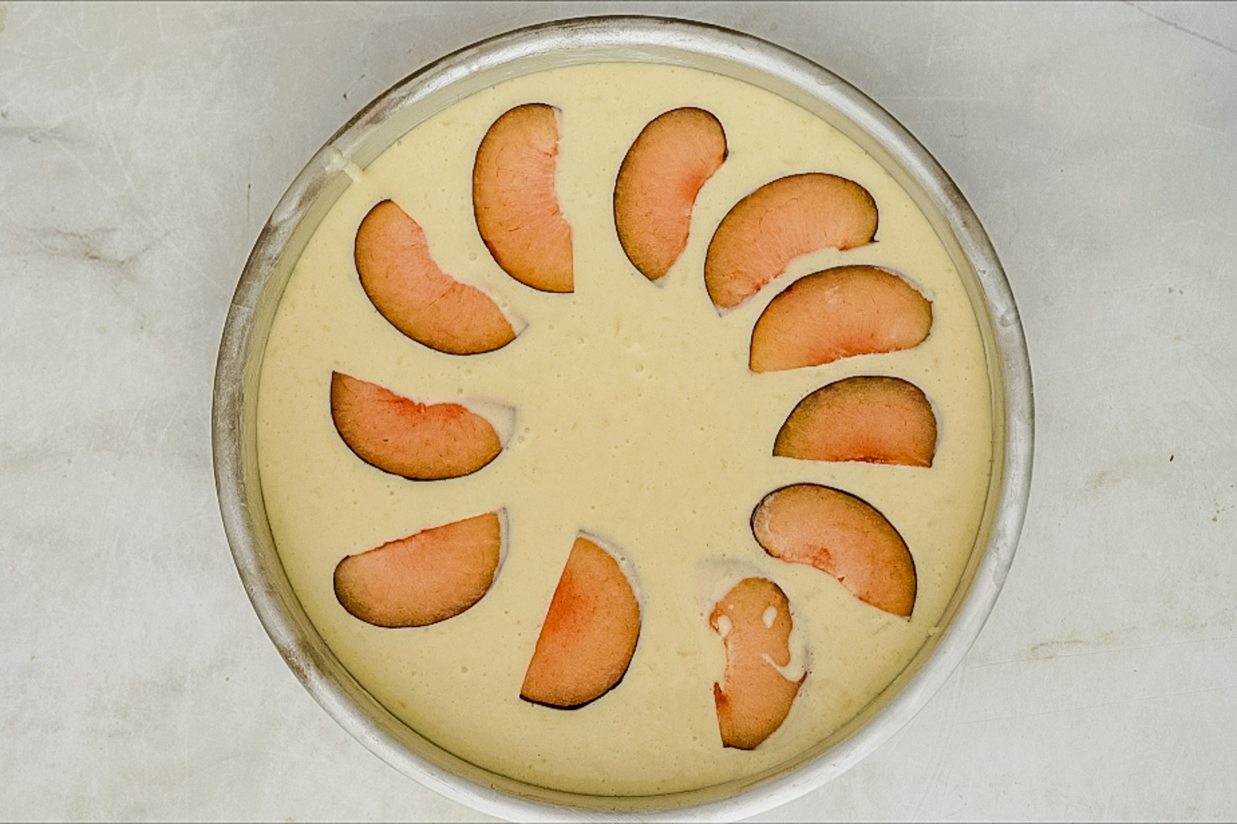 plum clafoutis decorated with sliced plums in baking pan ready to bake.