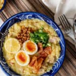 arroz caldo with toppings served in a blue bowl on a placemat.