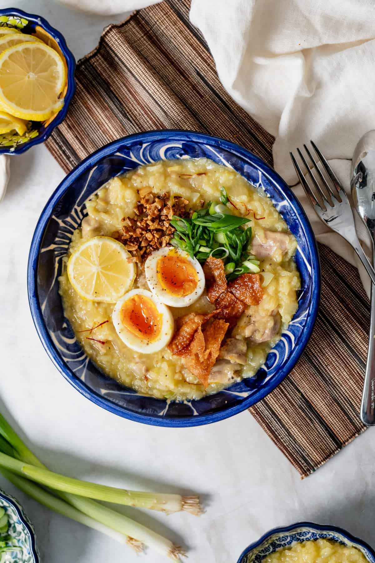 arroz caldo with toppings served in a blue bowl on a placemat.