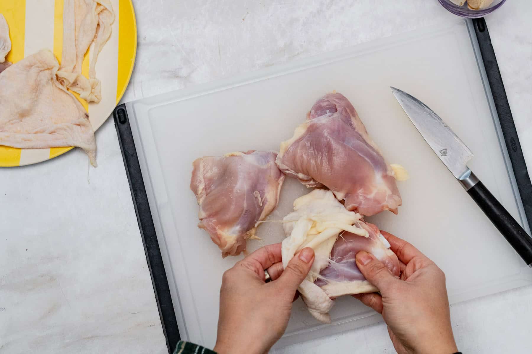removing chicken skin from chicken thigh on a cutting board.
