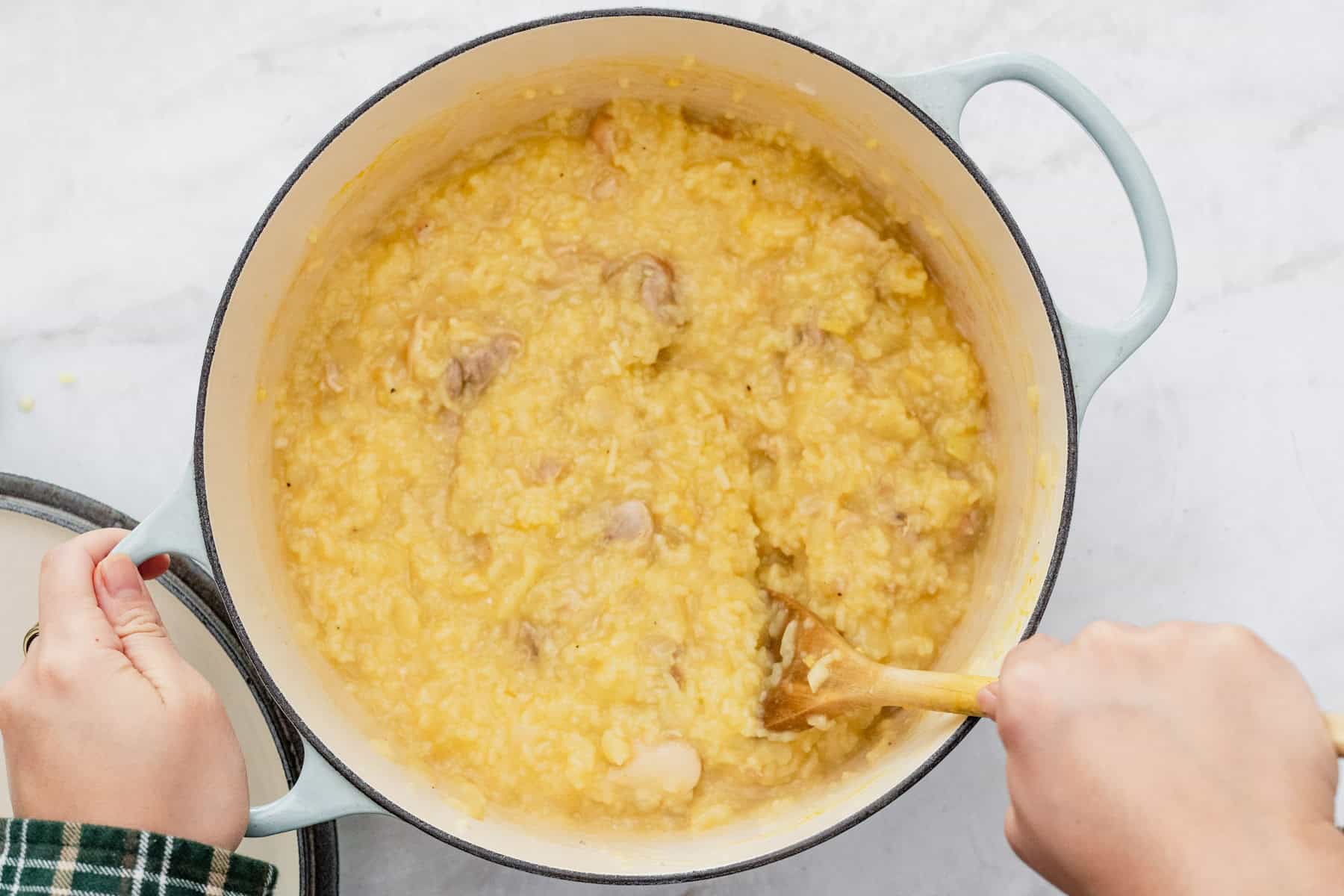stirring arroz caldo in a pot with a wooden spoon.