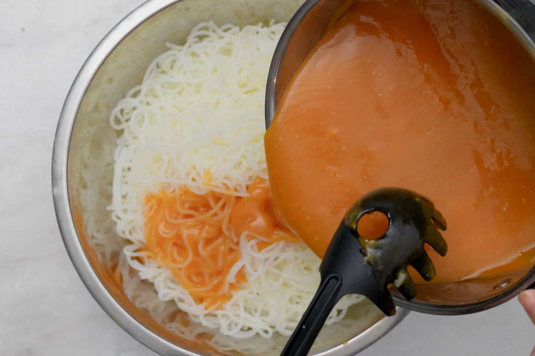 pouring palabok sauce in noodles.
