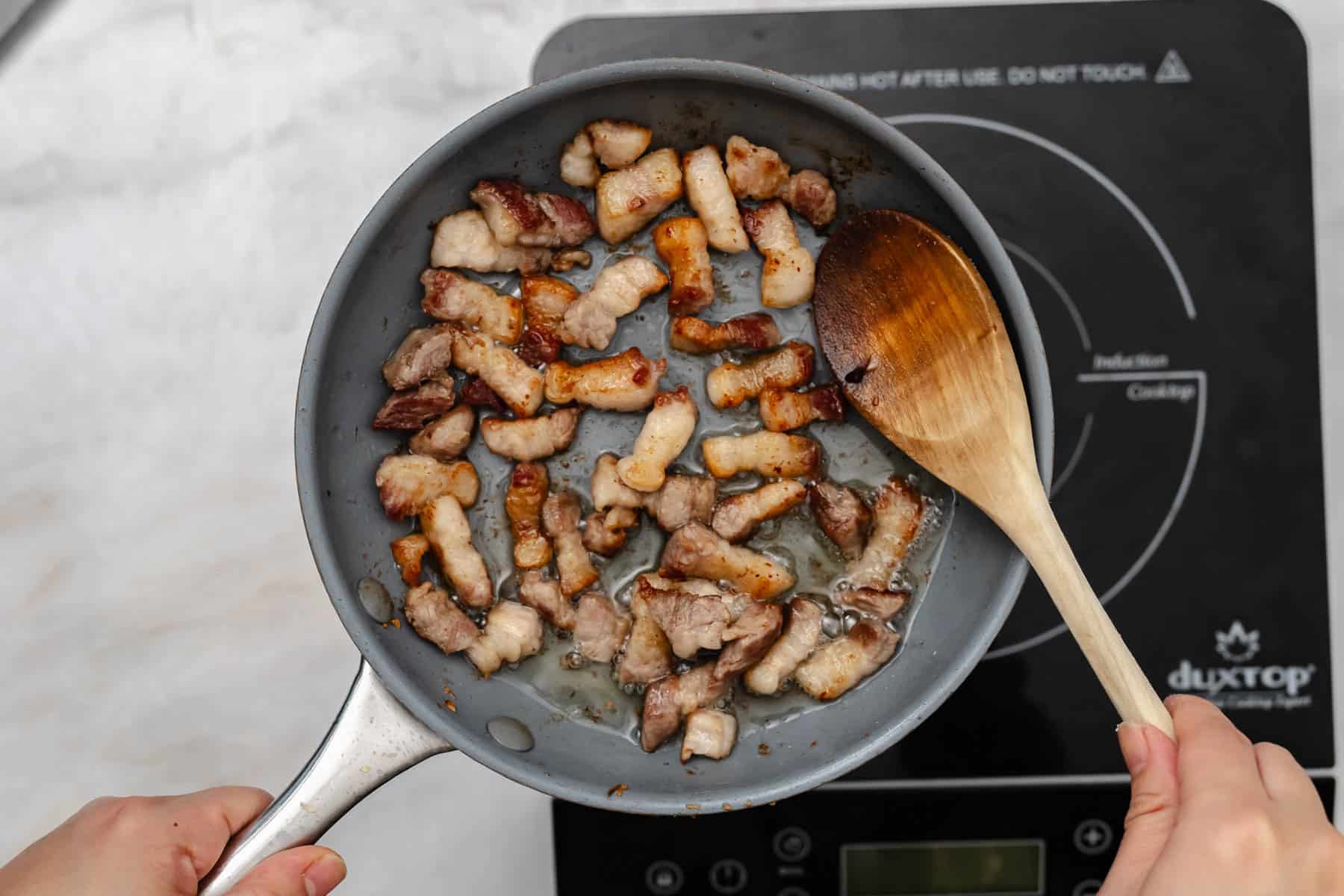 cooking pork belly in pan with wooden spoon.