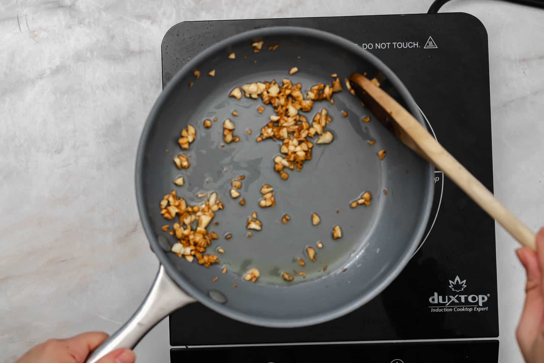 frying garlic in pan with wooden spoon.