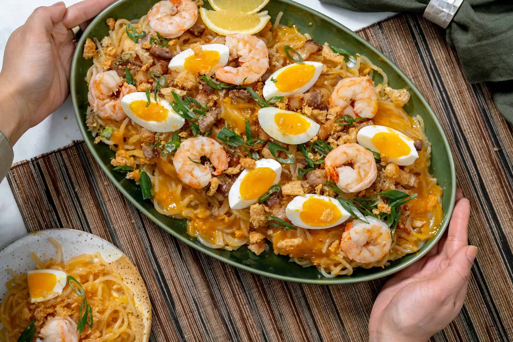 hands serving palabok in a green serving platter.