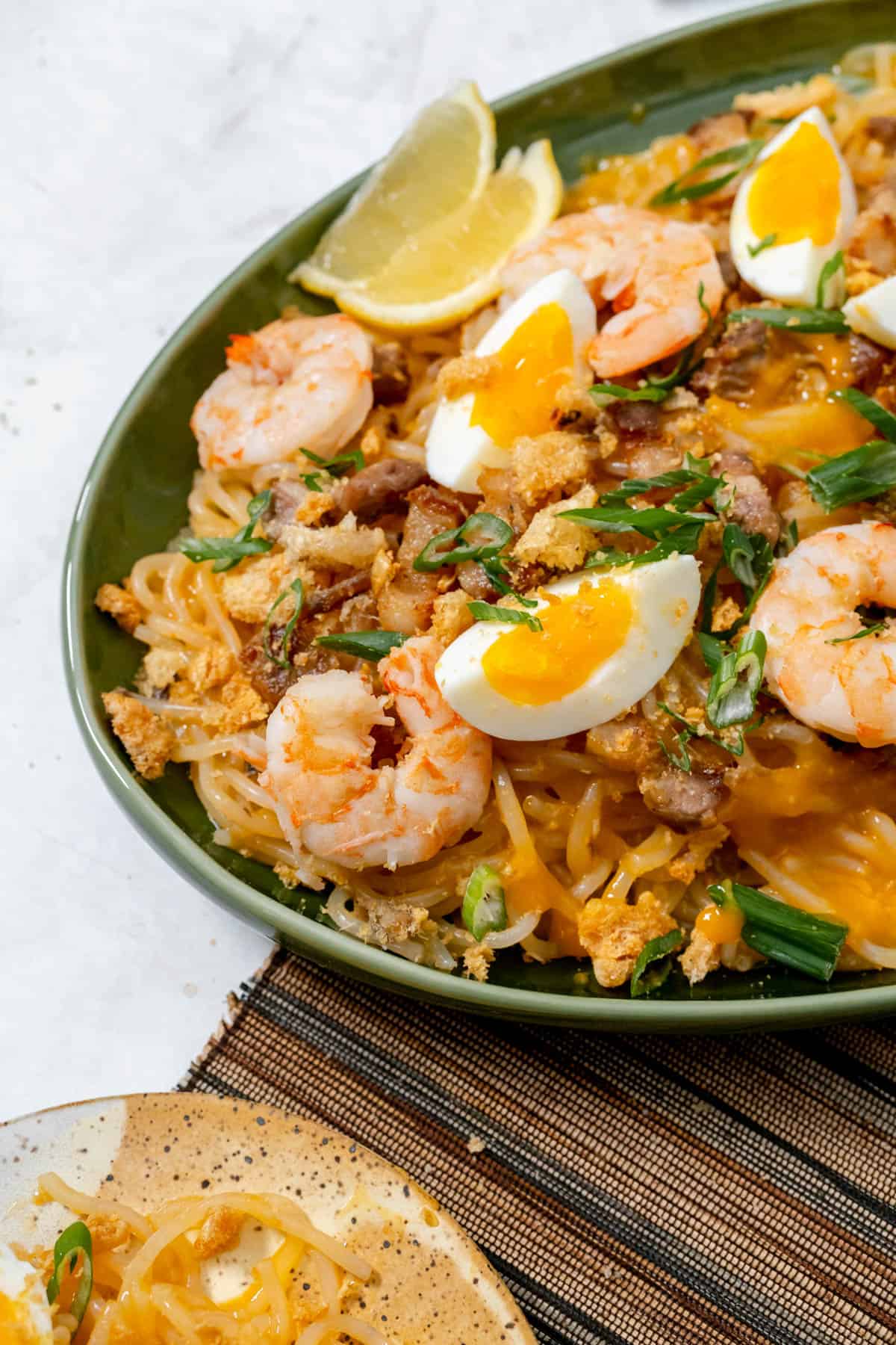 pancit palabok served with toppings on a green serving platter.