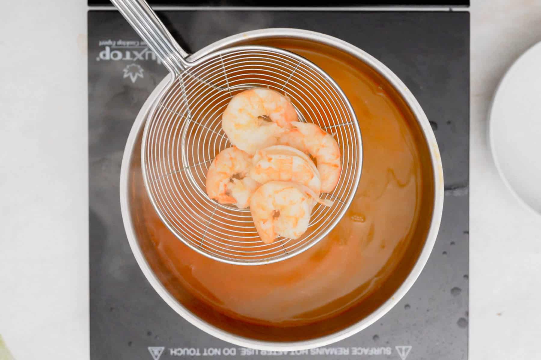 removing cooked poached shrimp from stock with spider tool.