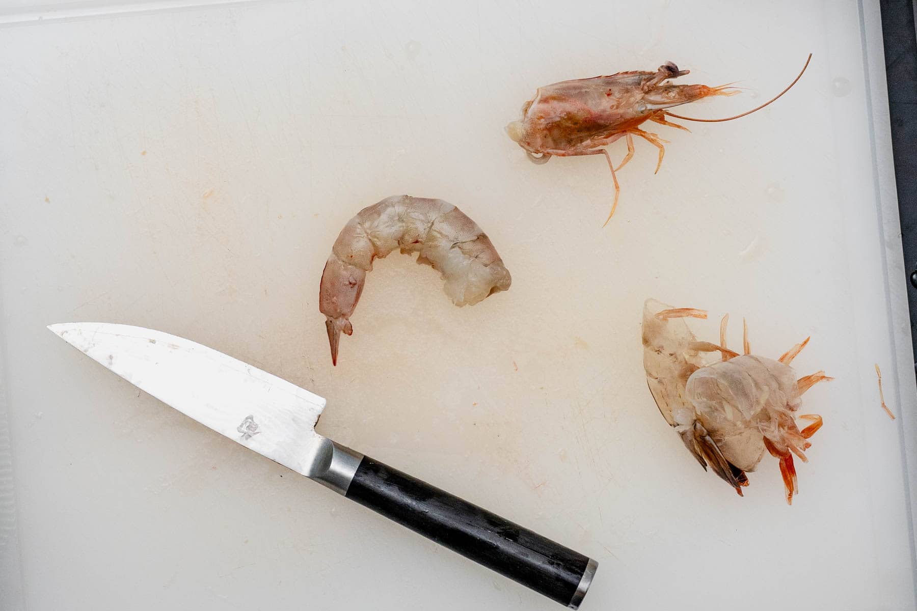 shrimp head, body , and shells on a cutting board with knife