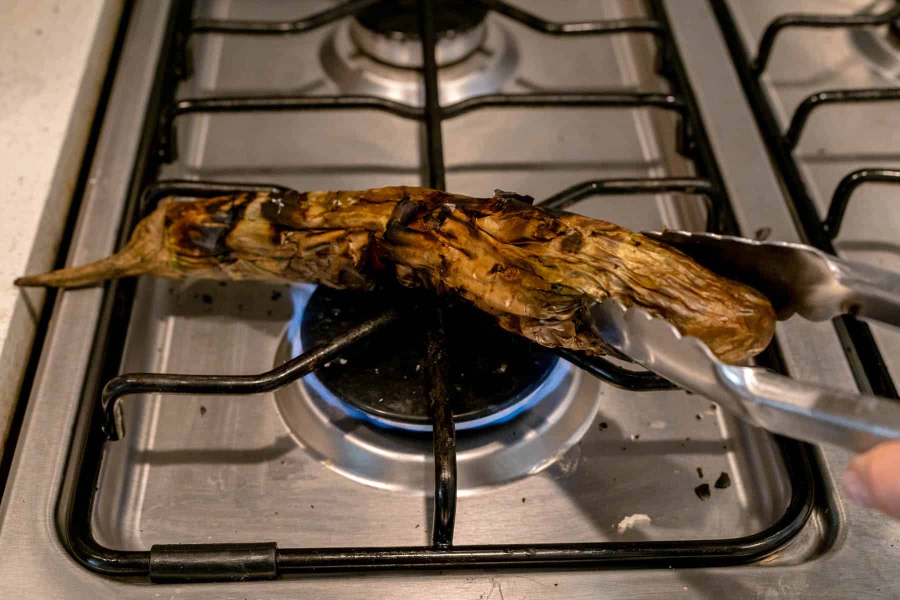 charring eggplant on gas flame, held by tongs.