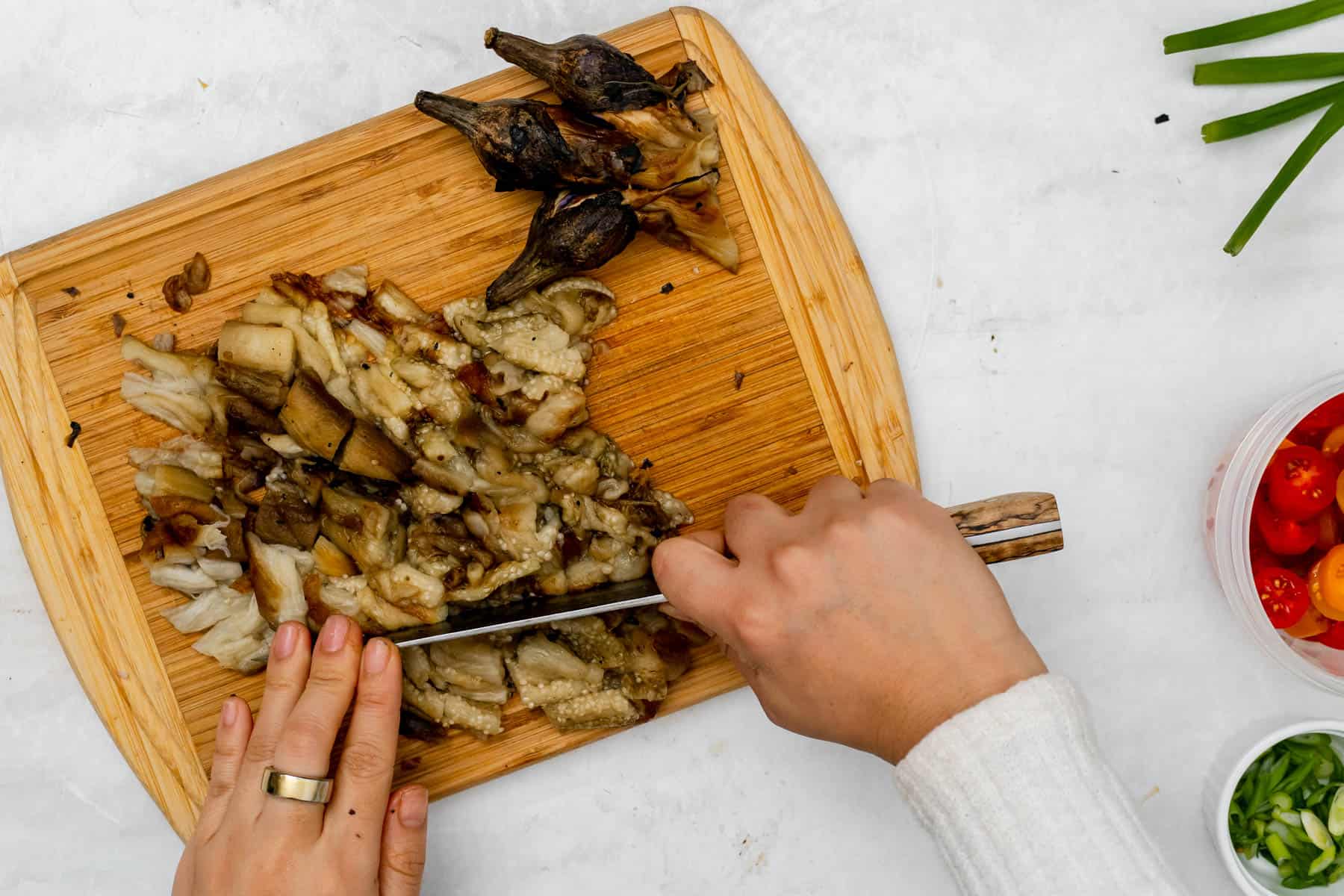 chopping charred eggplant with a knife on a chopping board.