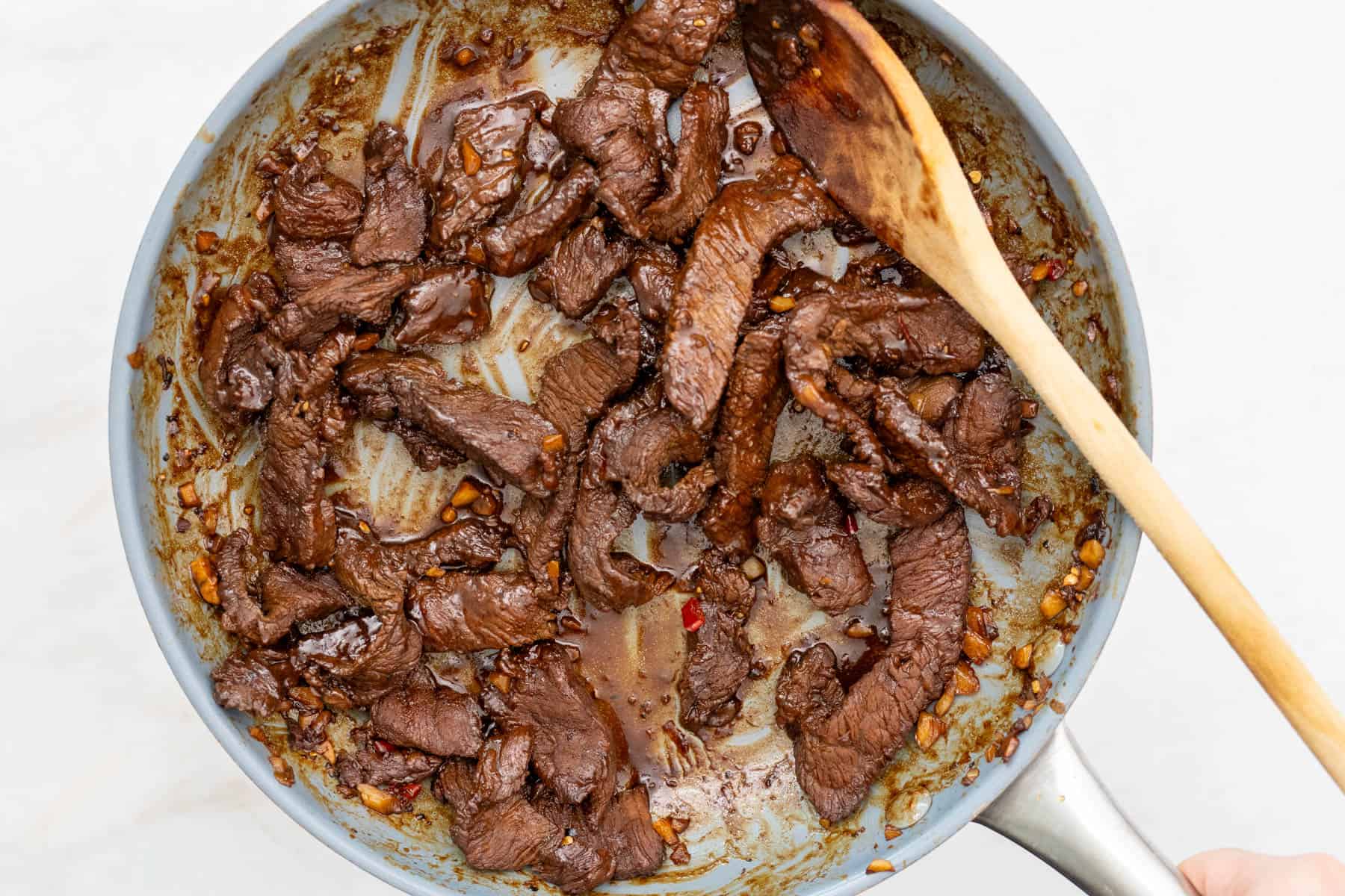 cooking beef tapa in a skillet with a wooden spoon.
