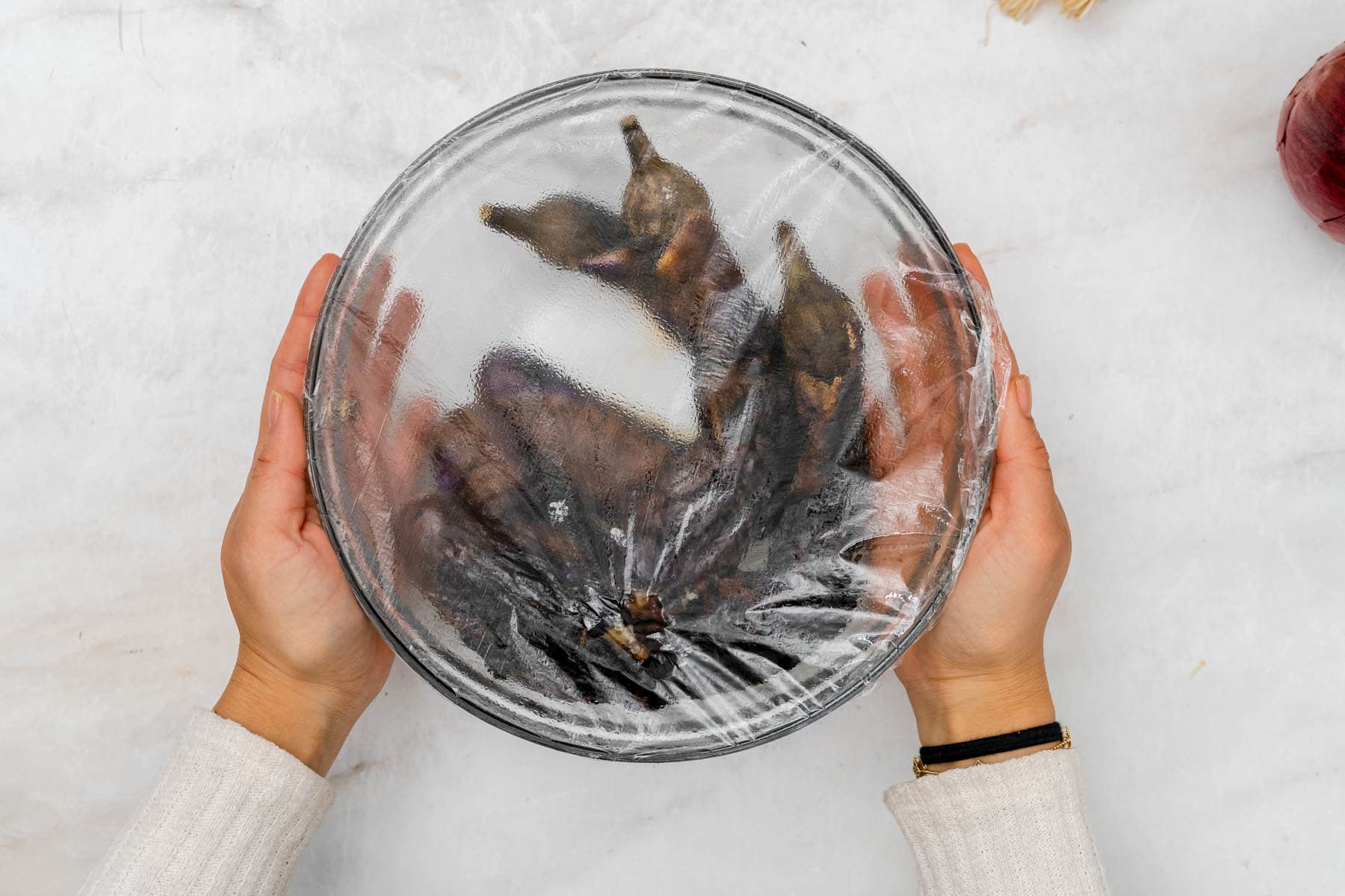 eggplants in bowl covered with plastic wrap to steam.