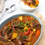 beef kaldereta served on a bowl with a fork and spoon on the left and a bowl of kaldereta with rice on the right.