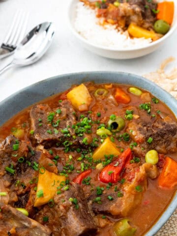 beef kaldereta served on a bowl with a fork and spoon on the left and a bowl of kaldereta with rice on the right.