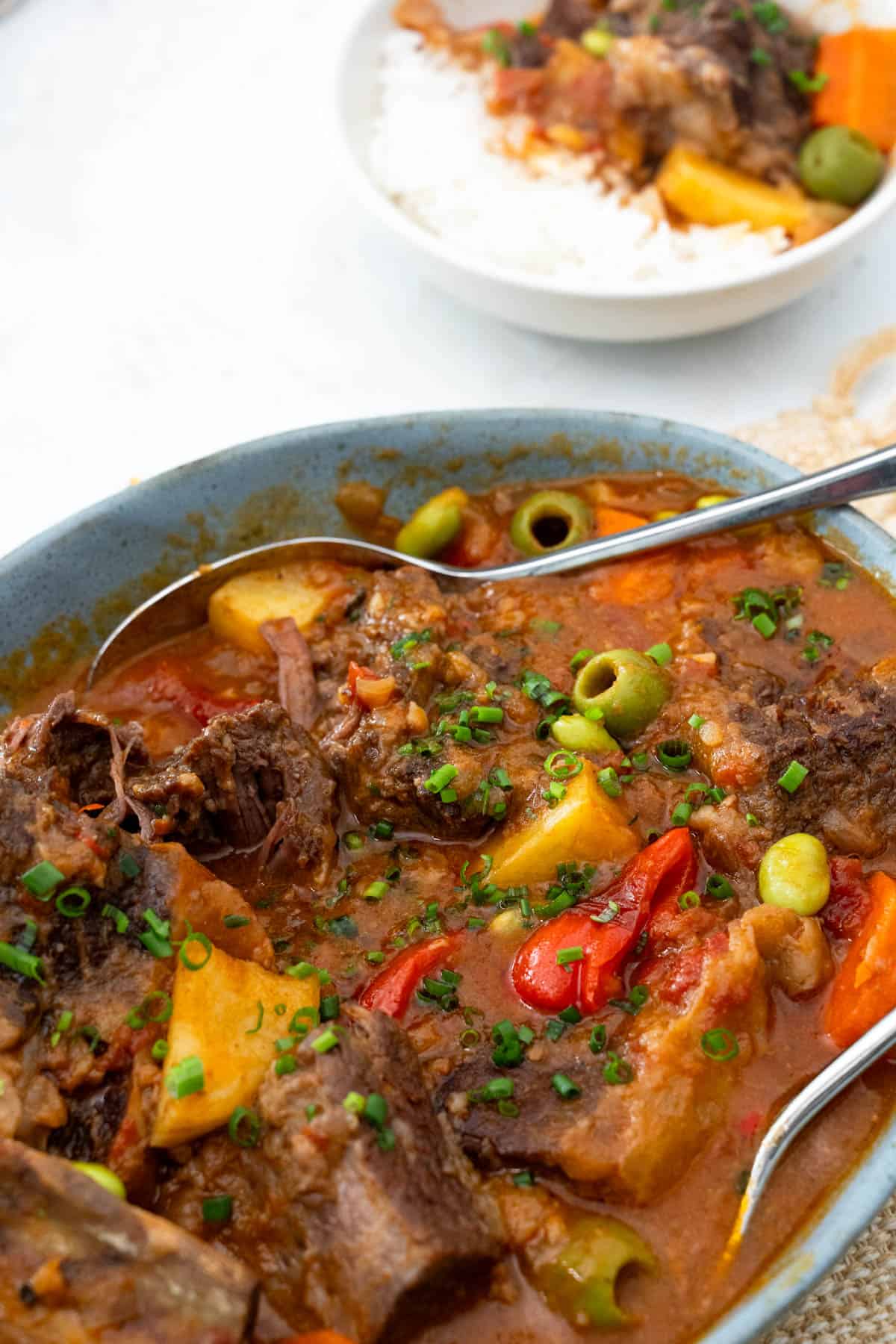 beef kaldereta served in a blou bowl with serving spoons and a bowl of beef kaldereta and rice on the top right.