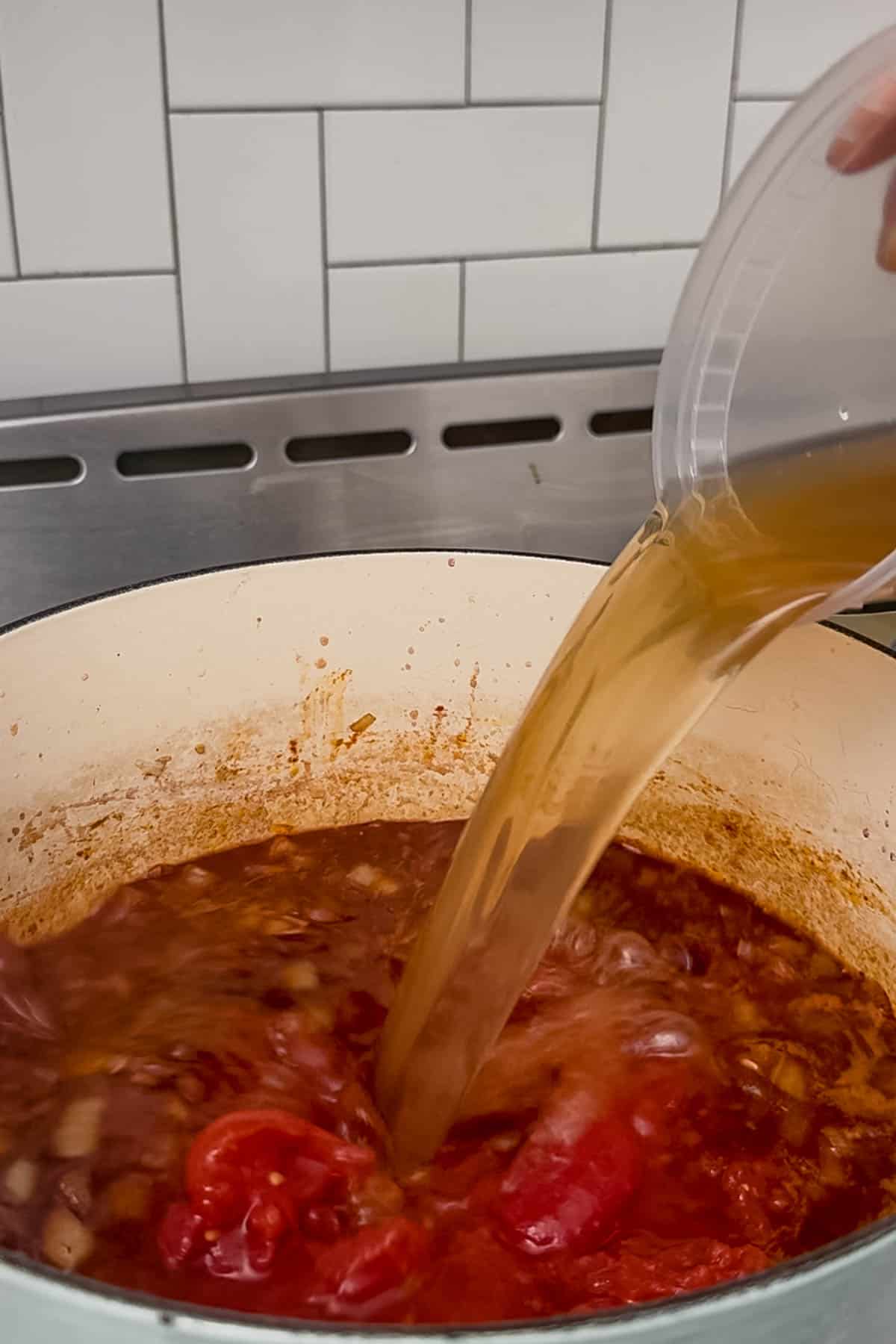 adding beef broth to the kaldereta sauce.