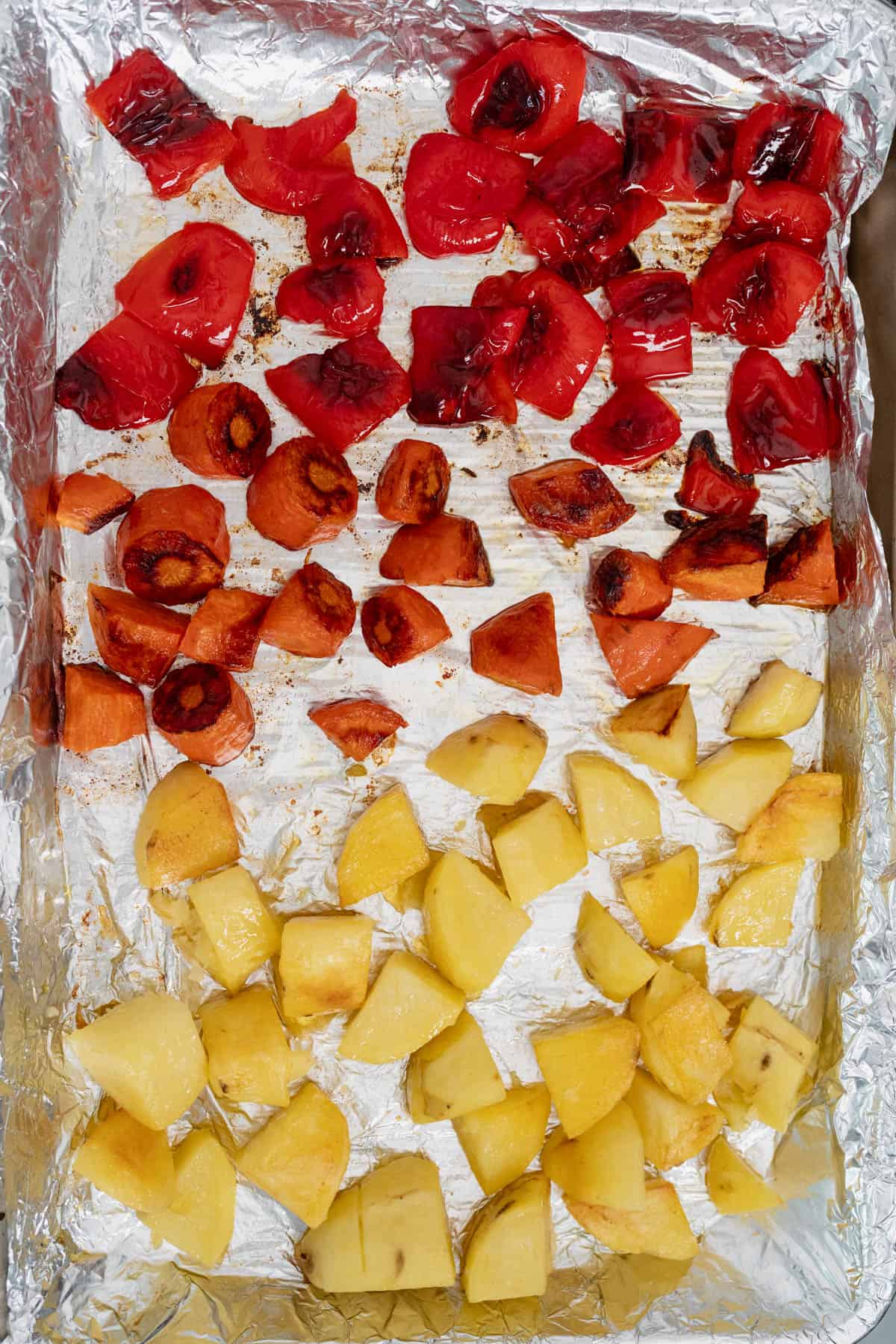 roasted carrots, peppers, and potatoes in a baking tray with foil.