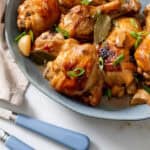 chicken adobo served on blue platter with blue serving utensils on bottom left.