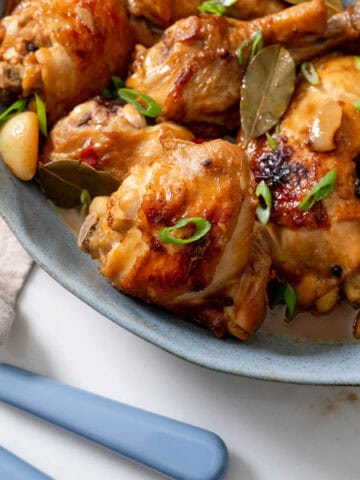 chicken adobo served on blue platter with blue serving utensils on bottom left.