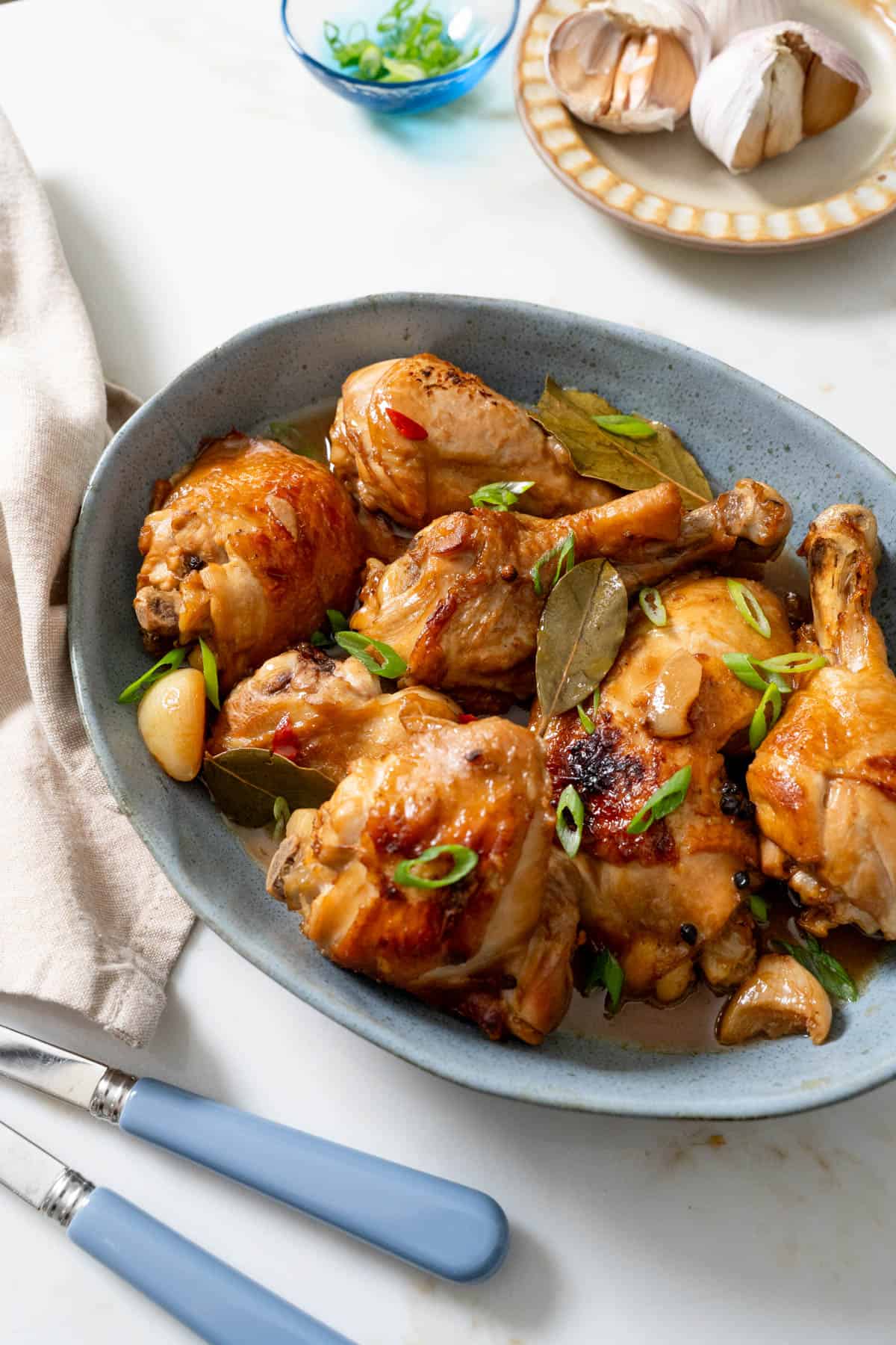 chicken adobo served on blue platter with blue serving utensils on bottom left.