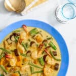 Colorful vegetable coconut milk stew with shrimp and eggplant in a blue bowl.