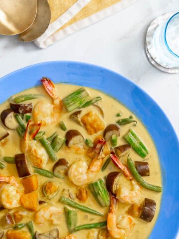 Colorful vegetable coconut milk stew with shrimp and eggplant in a blue bowl.