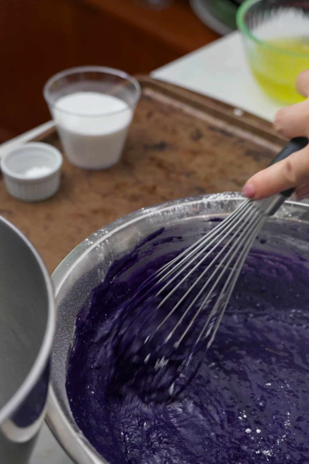 mixing ube cake batter in a bowl with a whisk.