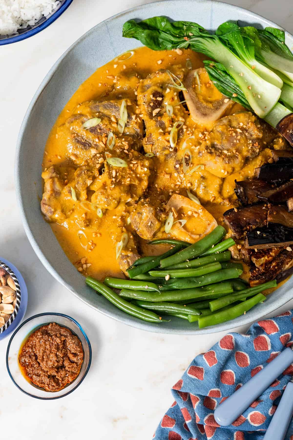 kare kare in a bowl with vegetable with napkin and serving ware on right hand side.