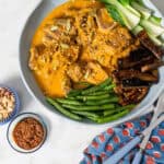 kare kare in a bowl with vegetable with napkin and serving ware on right hand side.
