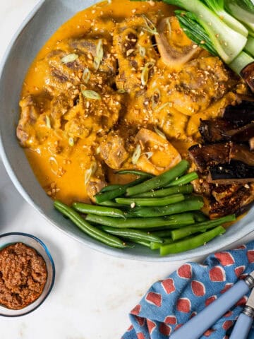 kare kare in a bowl with vegetable with napkin and serving ware on right hand side.