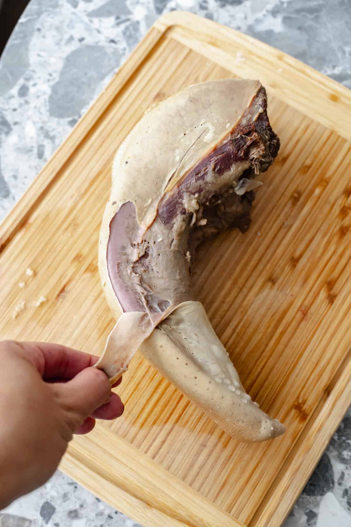 peeling beef lengua on a cutting board.