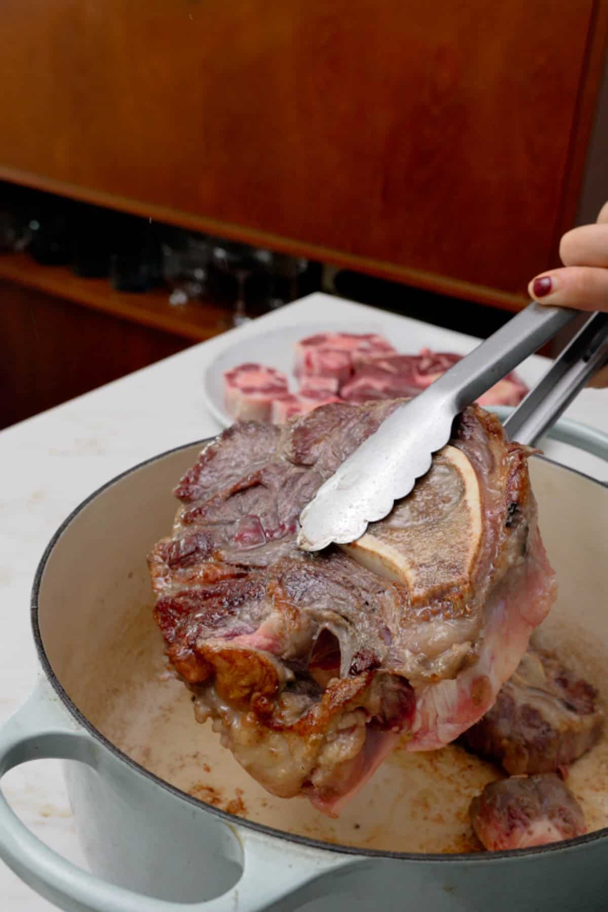 holding seared beef shank with tongs.