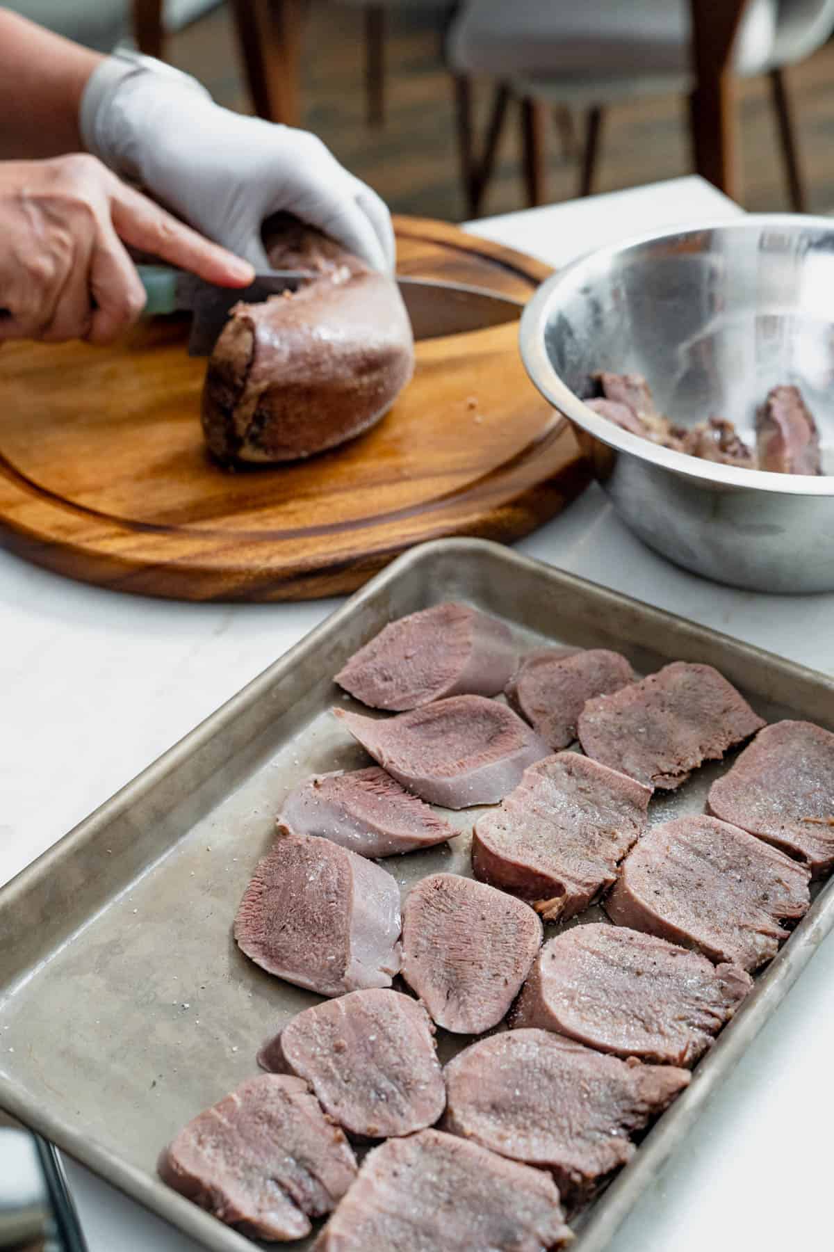 slicing lengua in background, sliced lengua on a tray in foreground.